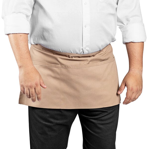 A man in a white shirt and brown Uncommon Chef waist apron standing at a counter.