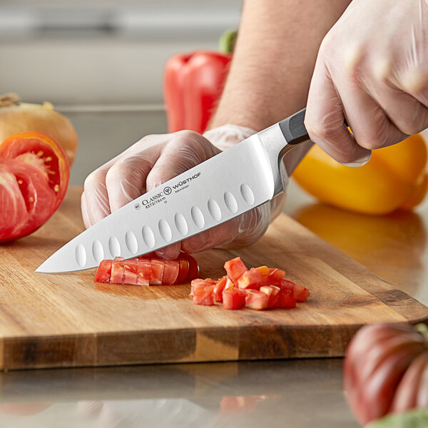 A person using a Wusthof Classic Cook's Knife to cut a tomato on a cutting board.