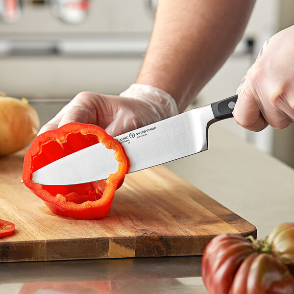 A person cutting a red pepper with a Wusthof Classic Cook's Knife.