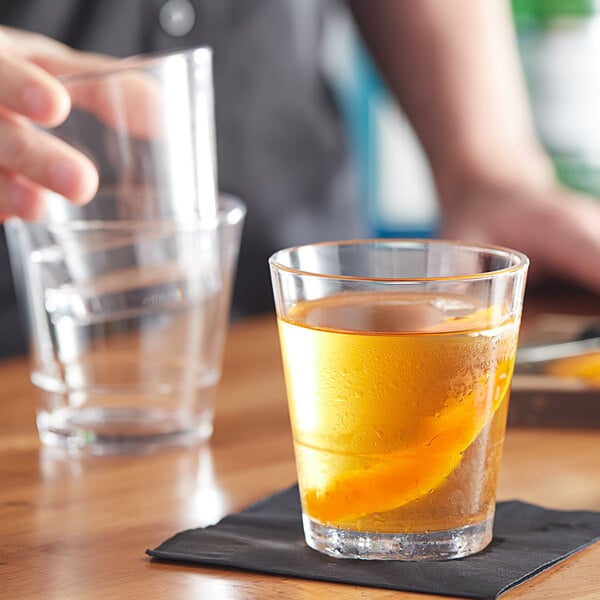 A hand pouring a drink into an Acopa Select Stackable Rocks glass on a table.