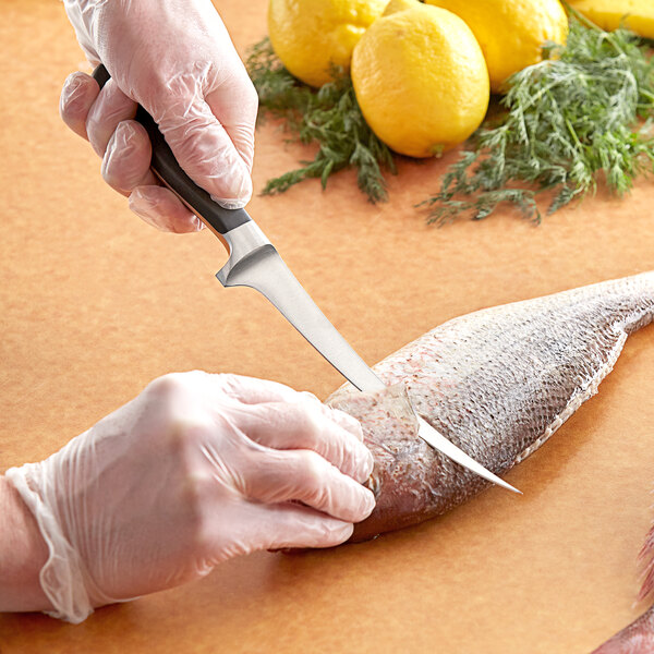 A person in white gloves using a Wusthof Classic fillet knife to cut a fish.