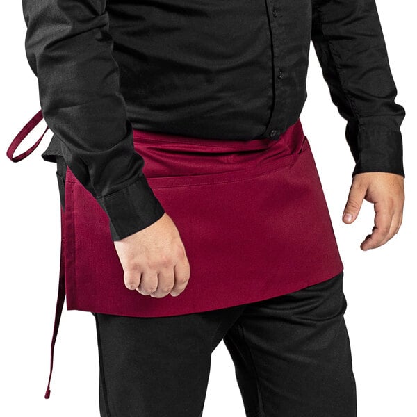 A man wearing a burgundy Uncommon Chef waist apron with three pockets.
