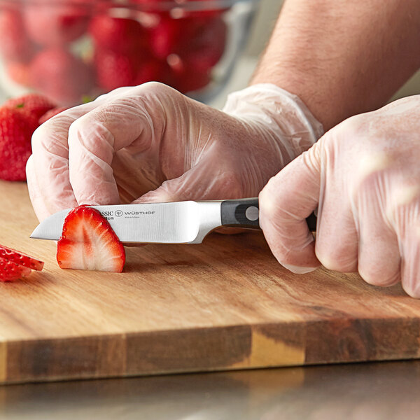 A person using a Wusthof Classic forged paring knife to cut a strawberry on a cutting board.