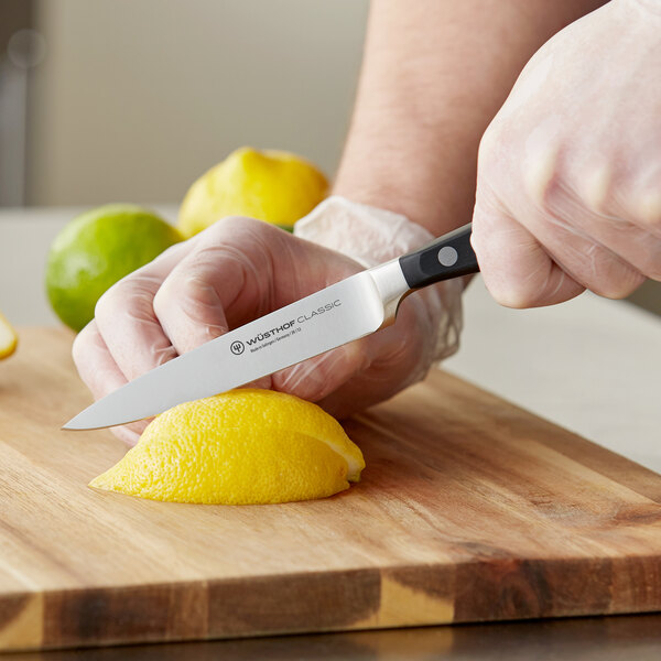 A person's hands using a Wusthof Classic forged utility knife to cut a lemon.