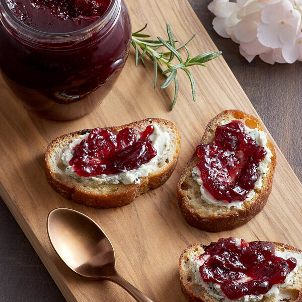 A wooden cutting board with a group of toasts and Dalmatia Sour Cherry Spread on top.