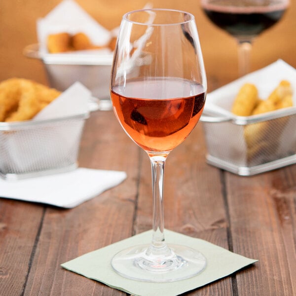 A Carlisle white wine glass filled with pink liquid on a table with food.