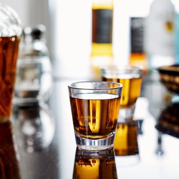 Two Carlisle Alibi shot glasses filled with brown liquid on a table.