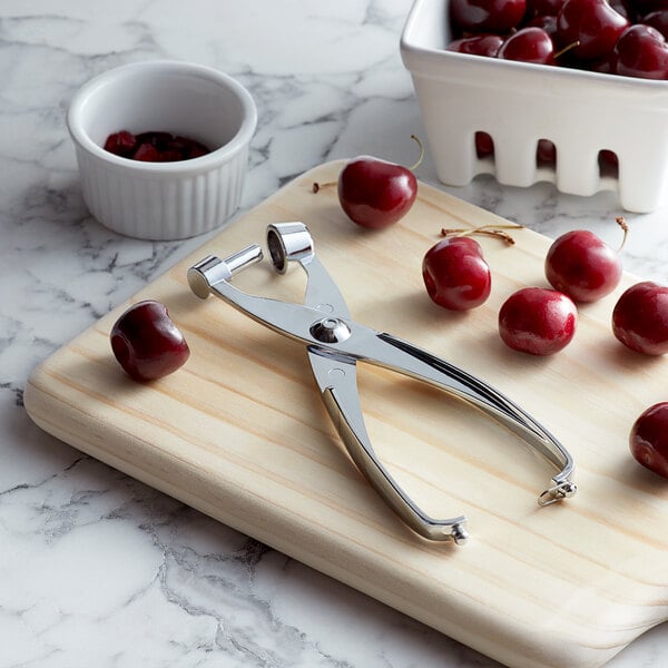 A Fox Run olive and cherry pit remover next to a white bowl of cherries.