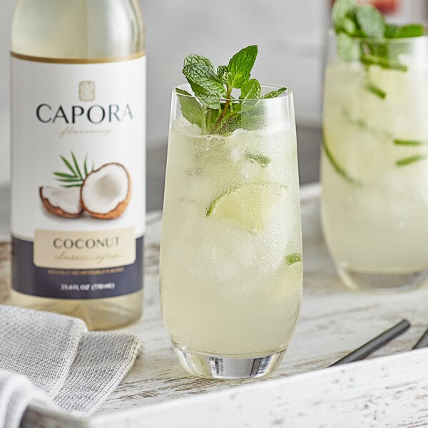 A glass of coconut and mint drink with ice and lime juice with Capora Coconut Flavoring Syrup on the side.