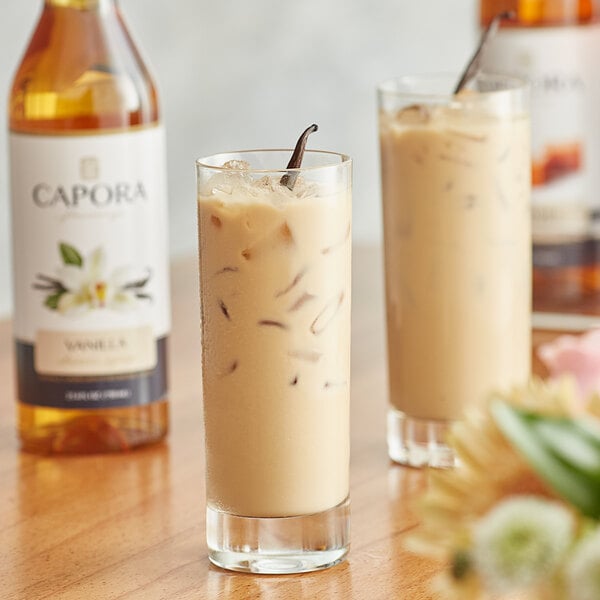A bottle of Capora Vanilla Flavoring Syrup on a table with two glasses of milkshake.