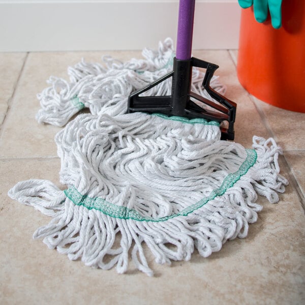A Carlisle wet mop with a green headband on the floor next to a bucket.