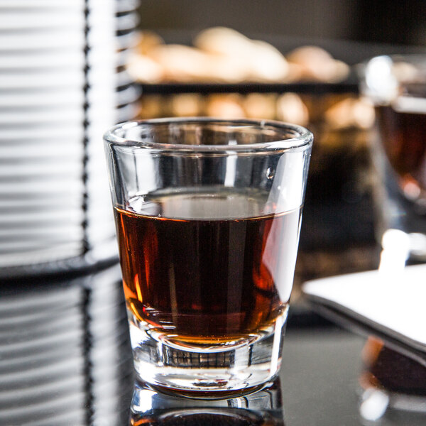 A Libbey shot glass filled with brown liquid on a table.
