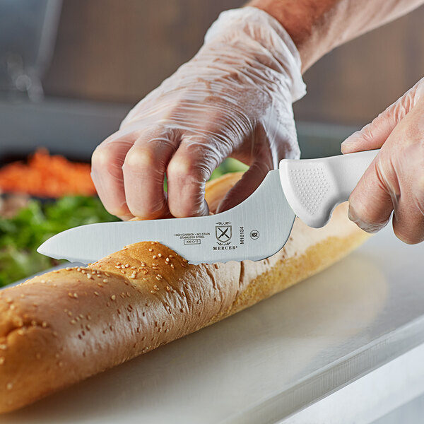 A person using a Mercer Culinary Ultimate White bread knife to cut a loaf of bread.