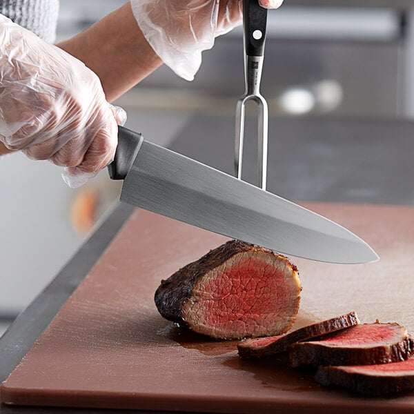 German butcher knife on a plastic cutting board preparing to cut into a large slab of beef
