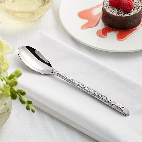 An Acopa stainless steel teaspoon on a white napkin next to a plate of chocolate cake with raspberries.