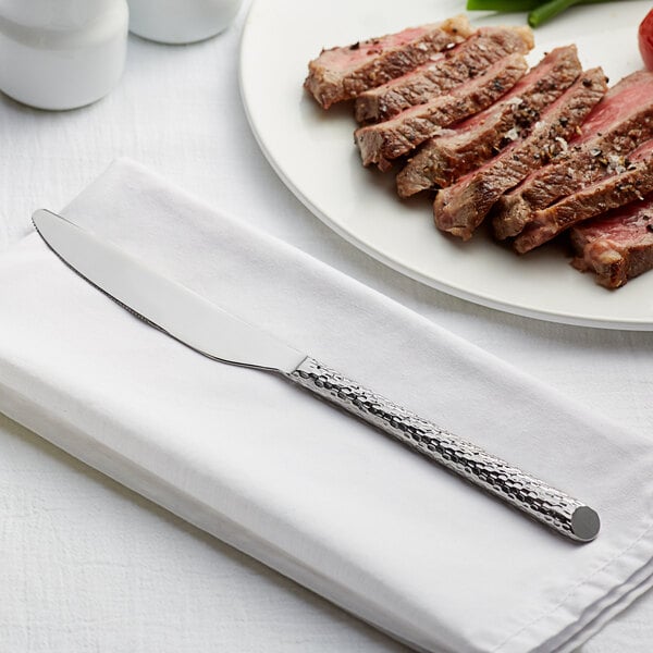An Acopa stainless steel dinner knife on a white napkin next to a steak.