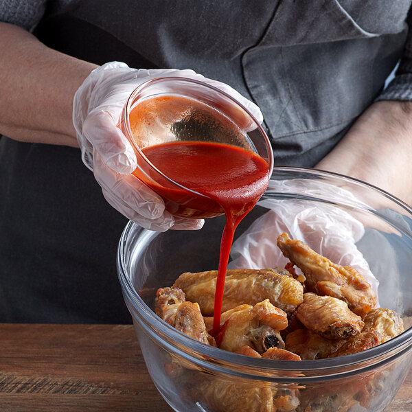 A person pouring TABASCO Cayenne Garlic Hot Sauce into a bowl of chicken wings.