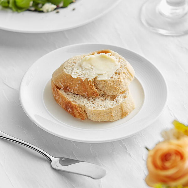 A white Acopa Liana porcelain plate with a piece of bread and a silver spoon on it.