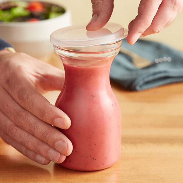 A hand holding a Choice polycarbonate carafe with a flat lid of pink liquid.