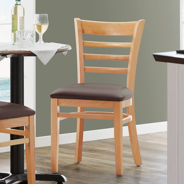 A Lancaster Table & Seating wooden ladder back chair with dark brown vinyl seat at a table in a restaurant.