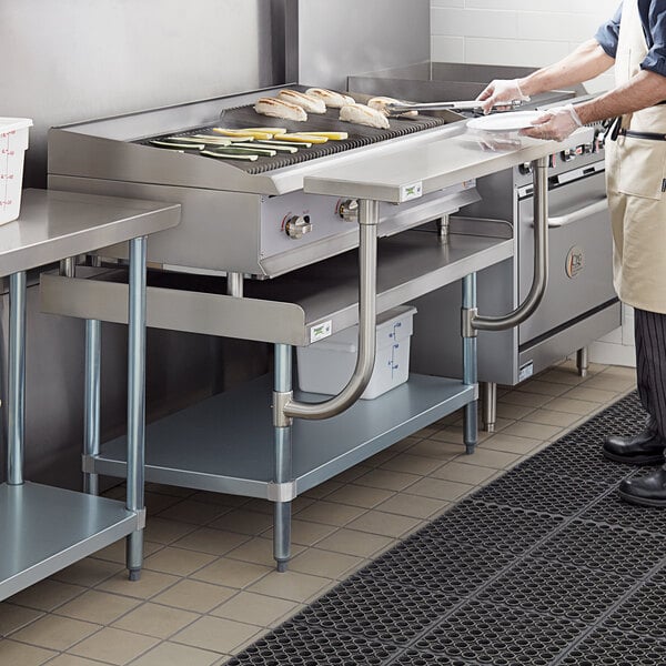 A man standing in a kitchen using a Regency stainless steel equipment stand with a grill.