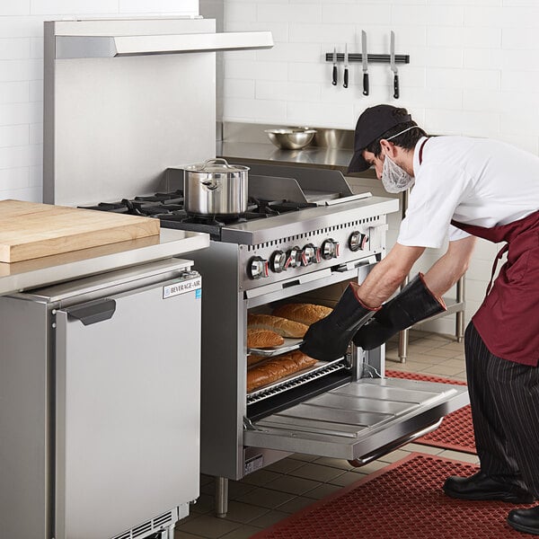 A chef in a professional kitchen putting food in a Cooking Performance Group range oven.