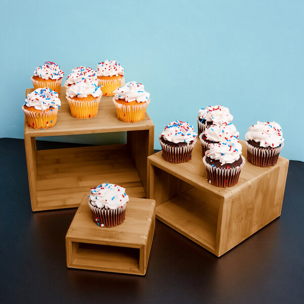 A set of three dark bamboo risers with cupcakes on them in a bakery display.