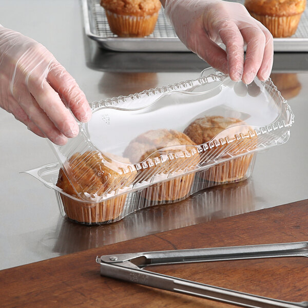 A person in gloves holding a clear plastic container of muffins.