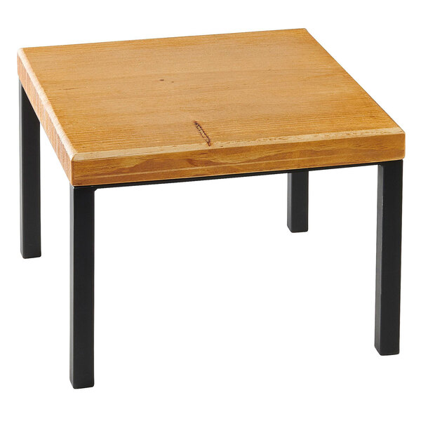 A Madera rustic pine square wood riser on a wooden table with black legs.