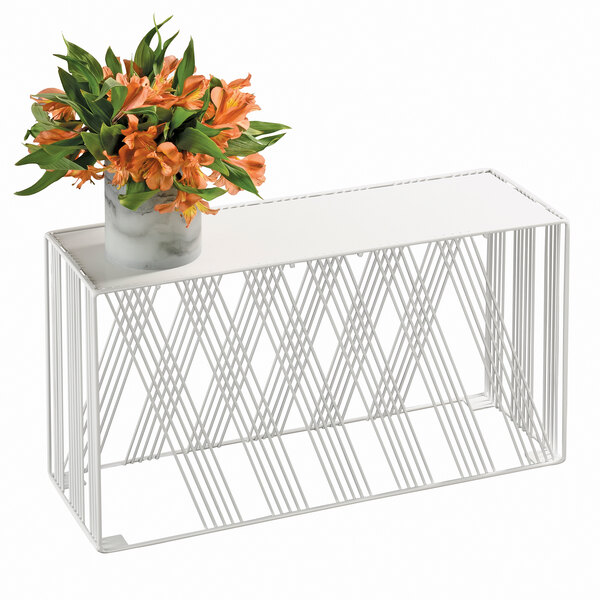 A white metal rectangular riser holding a vase of orange flowers on a table.