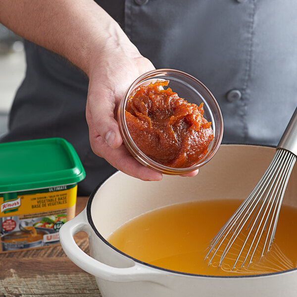 A person using a whisk to mix Knorr Ultimate Low Sodium Vegetable Bouillon in a pot.