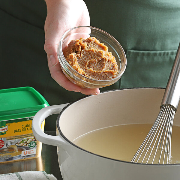 A person stirring a pot of Knorr Ultimate Clam Bouillon Base with a whisk.