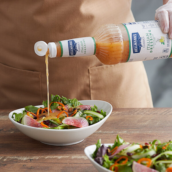 A person pouring Hellmann's Golden Italian Dressing into a bowl of salad.