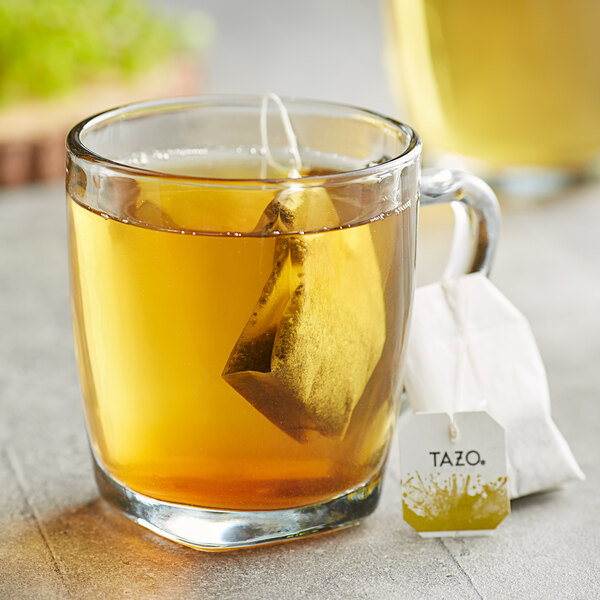 A glass mug of Tazo Green Ginger Tea with a tea bag in it.
