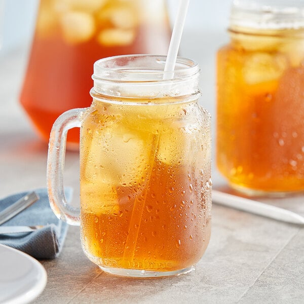 A glass mug with a straw filled with Lipton Peach Iced Tea.