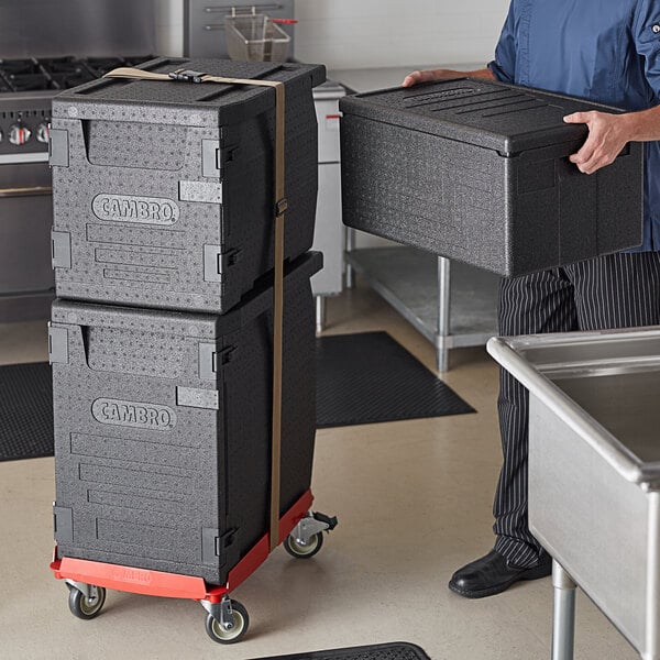 A man holding a stack of grey Cambro Cam GoBox food pan carriers.
