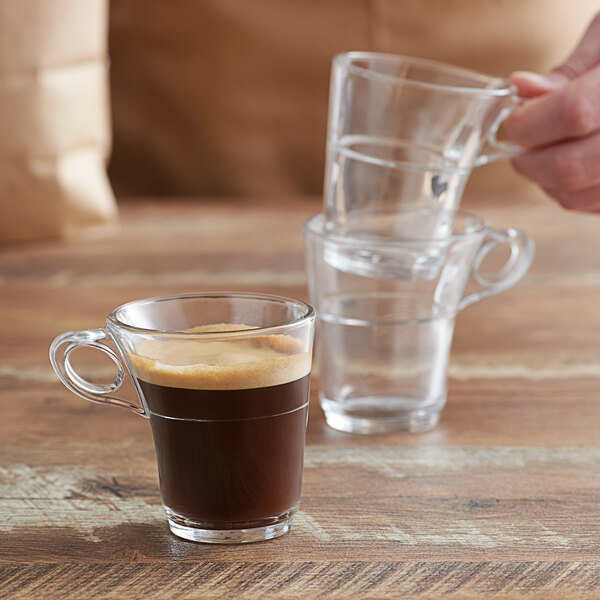 A person holding a Duralex Caprice stackable glass espresso mug filled with coffee.