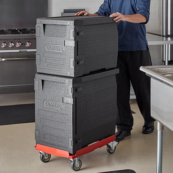 A man pushing a stack of black Cambro Cam GoBox pan carriers on a black Camdolly.