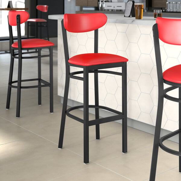 Lancaster Table & Seating Boomerang Series Black Finish Bar Stool with Red Vinyl Seat and Back on a counter in a cocktail bar.
