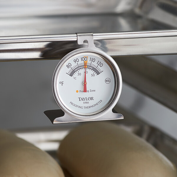 A Taylor 5986N dial proofing thermometer on a metal rack with dough.