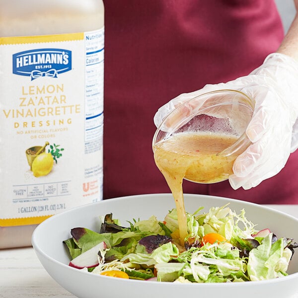 A person pouring Hellmann's Lemon Za'atar Vinaigrette dressing onto a bowl of salad.