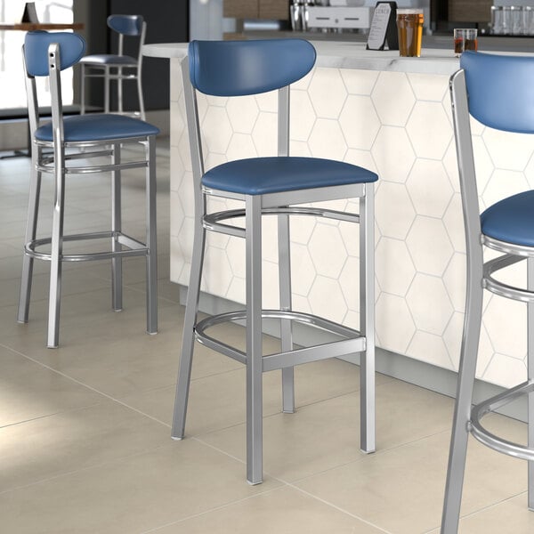 A group of Lancaster Table & Seating Boomerang Series bar stools with blue seats next to a white counter.