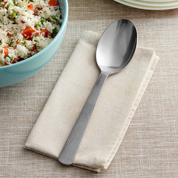 An American Metalcraft hammered stainless steel solid spoon on a napkin next to a bowl of rice.