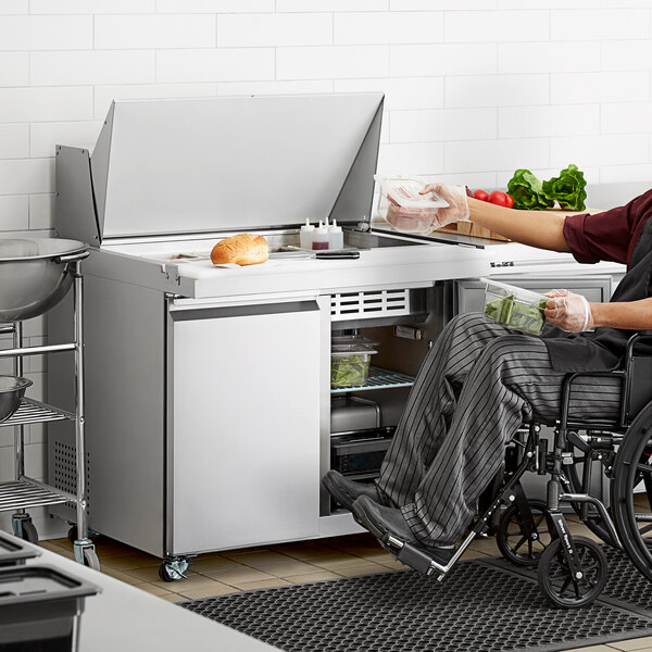 A man in a wheelchair using an Avantco ADA height sandwich prep table to prepare vegetables.
