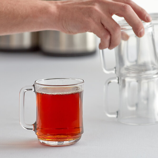A hand pouring brown liquid into a Duralex stackable glass mug.