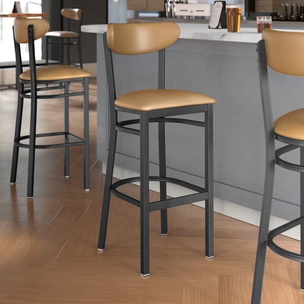 Three Lancaster Table & Seating Boomerang Series bar stools with light brown vinyl seats and backs next to a counter.