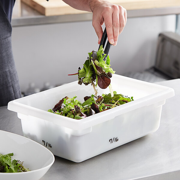A hand using tongs to place lettuce in a white Vigor food storage container.