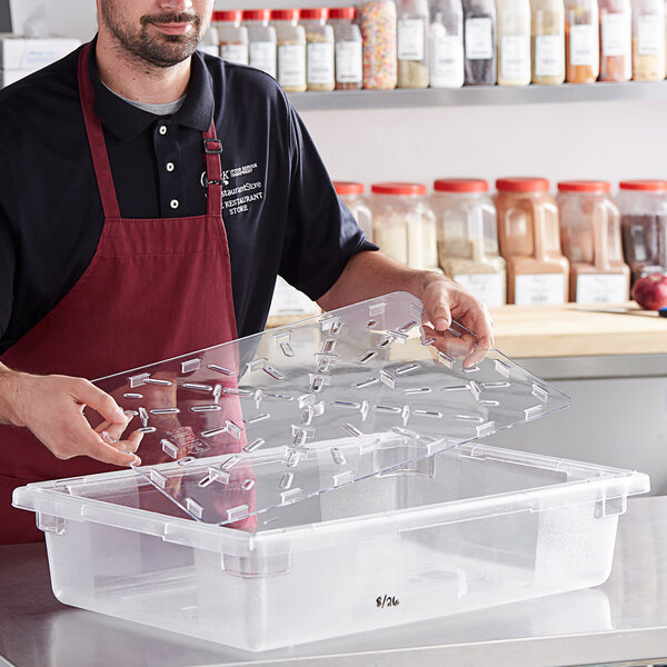 A man in an apron holding a clear polycarbonate tray over a clear polycarbonate food box.