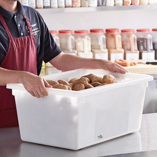 A man in an apron holding a white Vigor polyethylene food storage container full of potatoes.