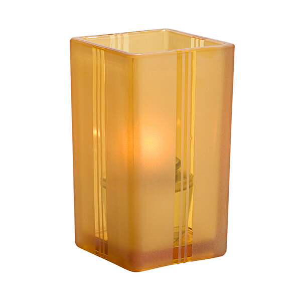 A Hollowick amber glass square votive holder with a lit candle inside.
